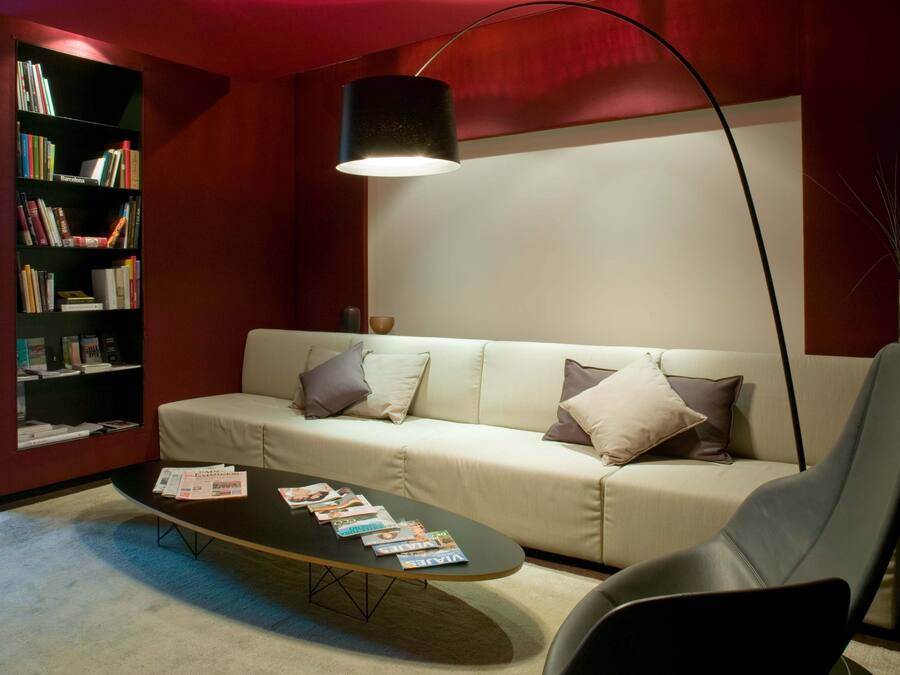 Uma sala de estar moderna com um sofá, uma mesa de centro com revistas, uma estante de livros e um abajur.