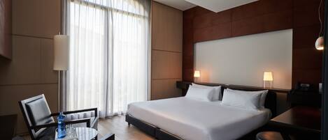 A hotel room with a large bed, a desk, a chair, a lamp, and a window with curtains.