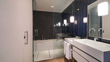 Un baño moderno con cabina de ducha de vidrio, un espejo grande y un tocador blanco con lavamanos doble.