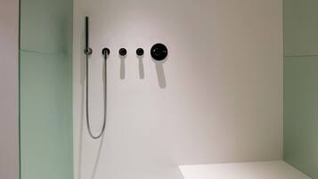 A modern bathroom with a white bathtub, a shower with a handheld showerhead, and a wall-mounted control panel.