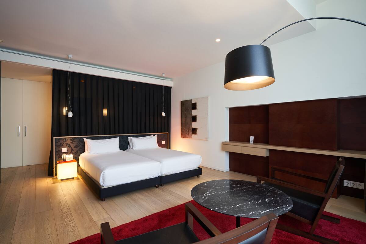 Ein modernes Hotelzimmer mit einem großen Bett, einem runden Tisch und einer dunklen Deckenleuchte.