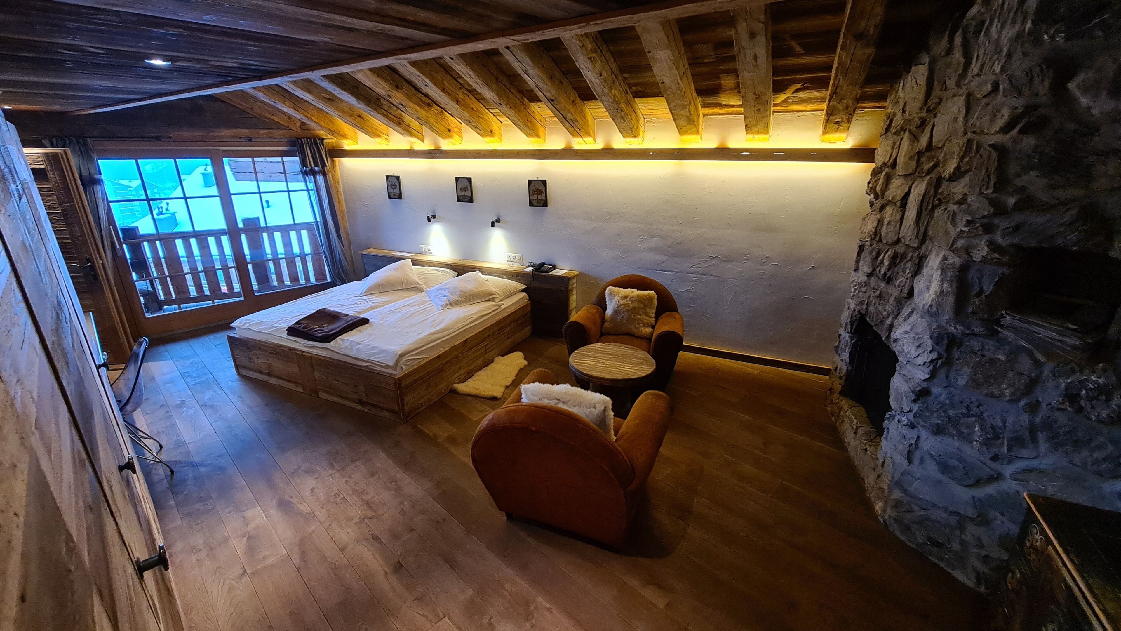 Ein gemütliches Zimmer mit einem hölzernen Bett, einem kleinen Tisch, zwei Stühlen und einer Steinwand.