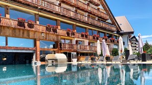 A hotel with a pool, outdoor seating, and a wooden balcony with flower boxes. - Hôtel de l'Etrier (Crans-Montana)