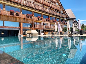 Un hotel con piscina, mobiliario exterior y un balcón de madera con jardineras.