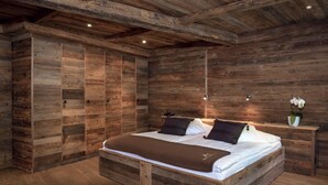 A wooden bedroom with a large bed, wooden wardrobe, and a nightstand with a vase of flowers. - Hôtel de l'Etrier (Crans-Montana)