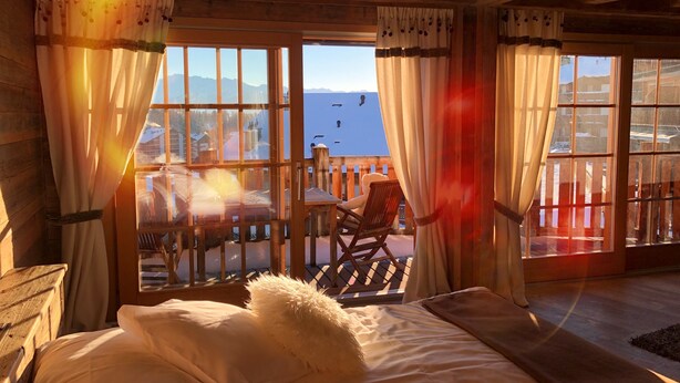 A cozy room with a bed, a chair, and large windows offering a view of mountains and a lake. - Hôtel de l'Etrier (Crans-Montana)