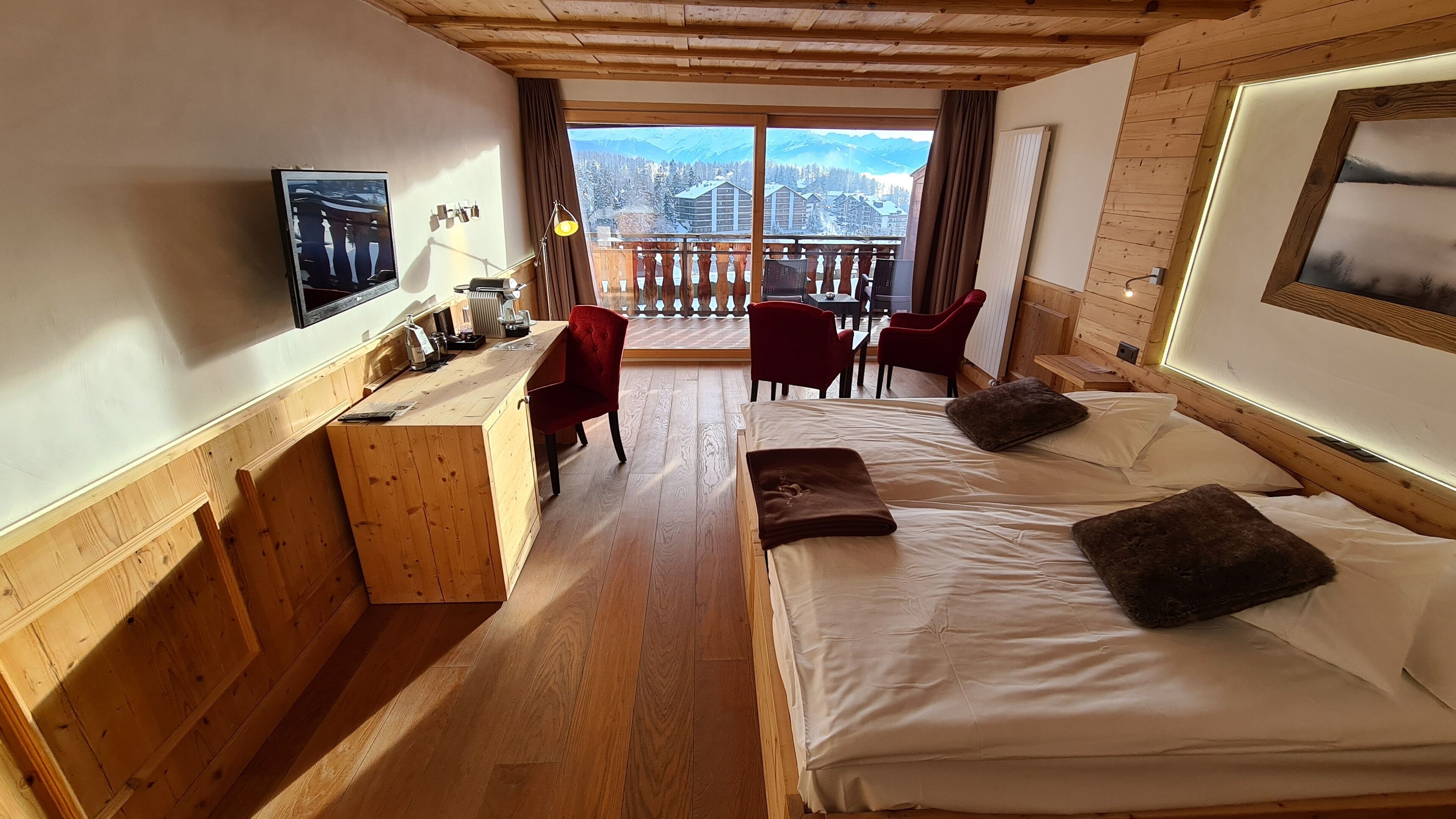 Una stanza in legno con un letto, una scrivania e una sedia. Si vede una finestra con vista sulle montagne.