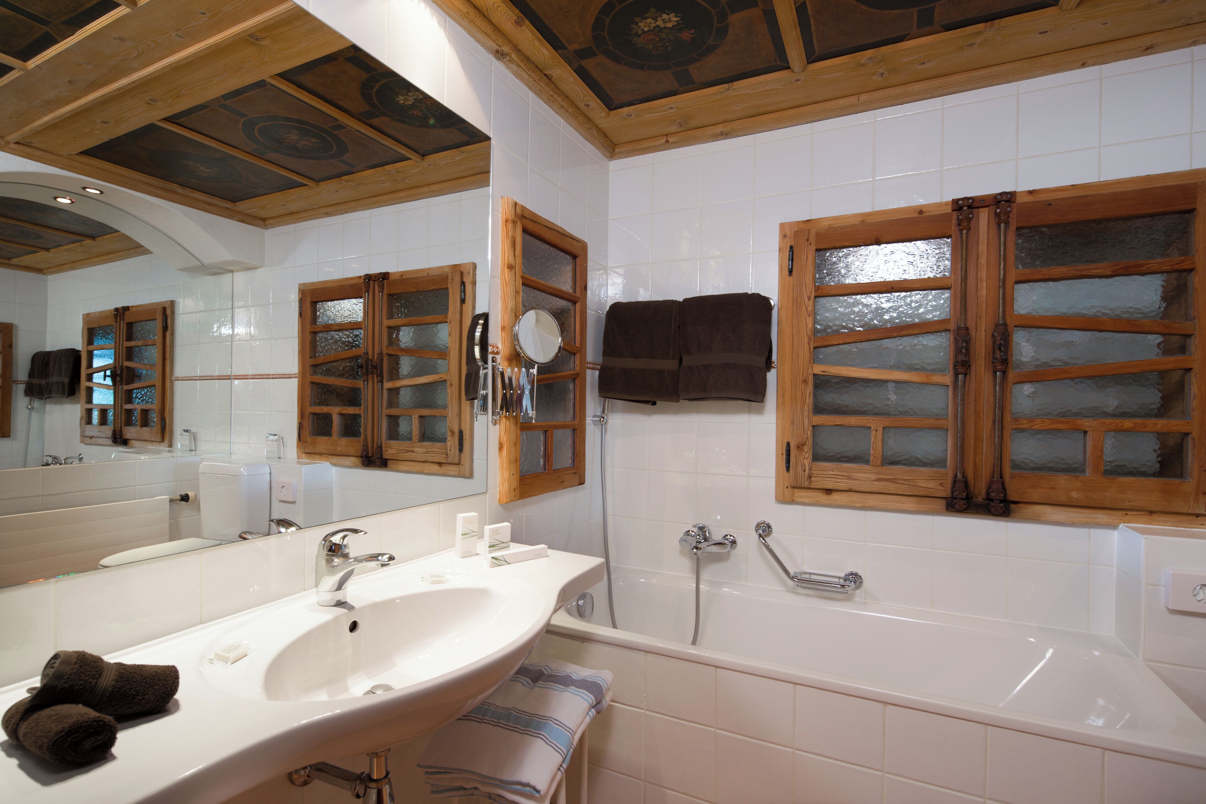Un baño con lavamanos doble, bañera, ventanas de madera y un espejo grande.