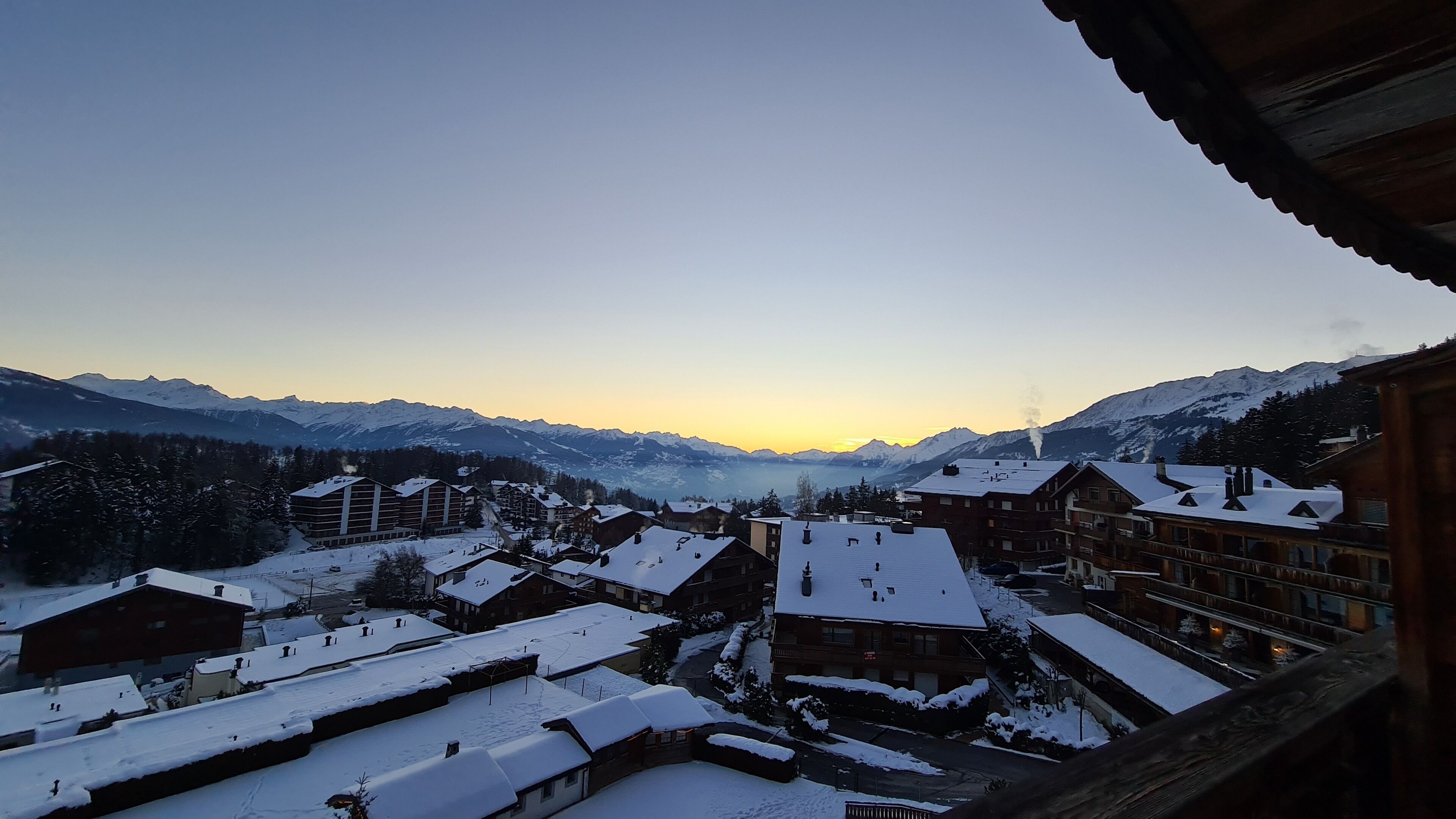 A snow-covered mountain town with buildings and a view of snow-capped mountains in the background.
