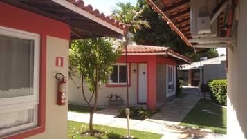 Un pequeño edificio de una sola planta con fachada roja y blanca, tejado de tejas y un pequeño jardín con una palmera y un extintor colgado en la pared.