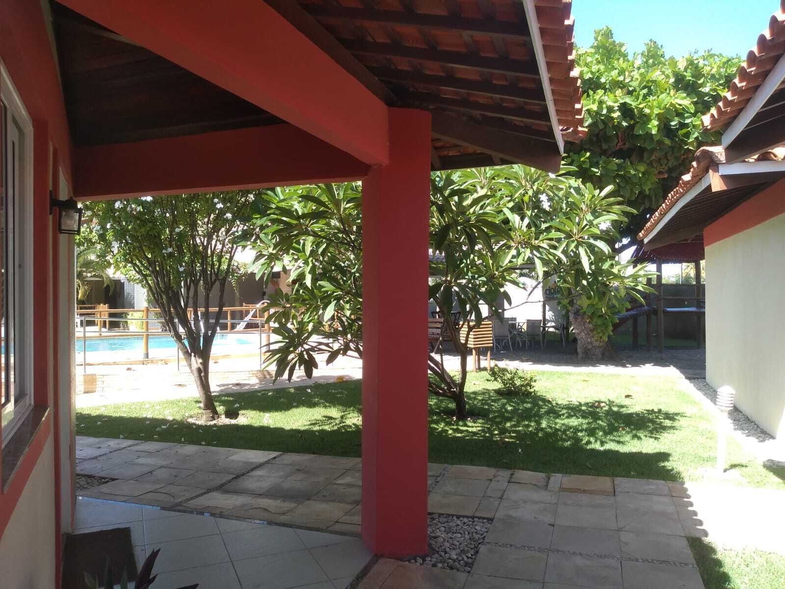 A covered patio area with a pool in the background, surrounded by greenery and a small garden.