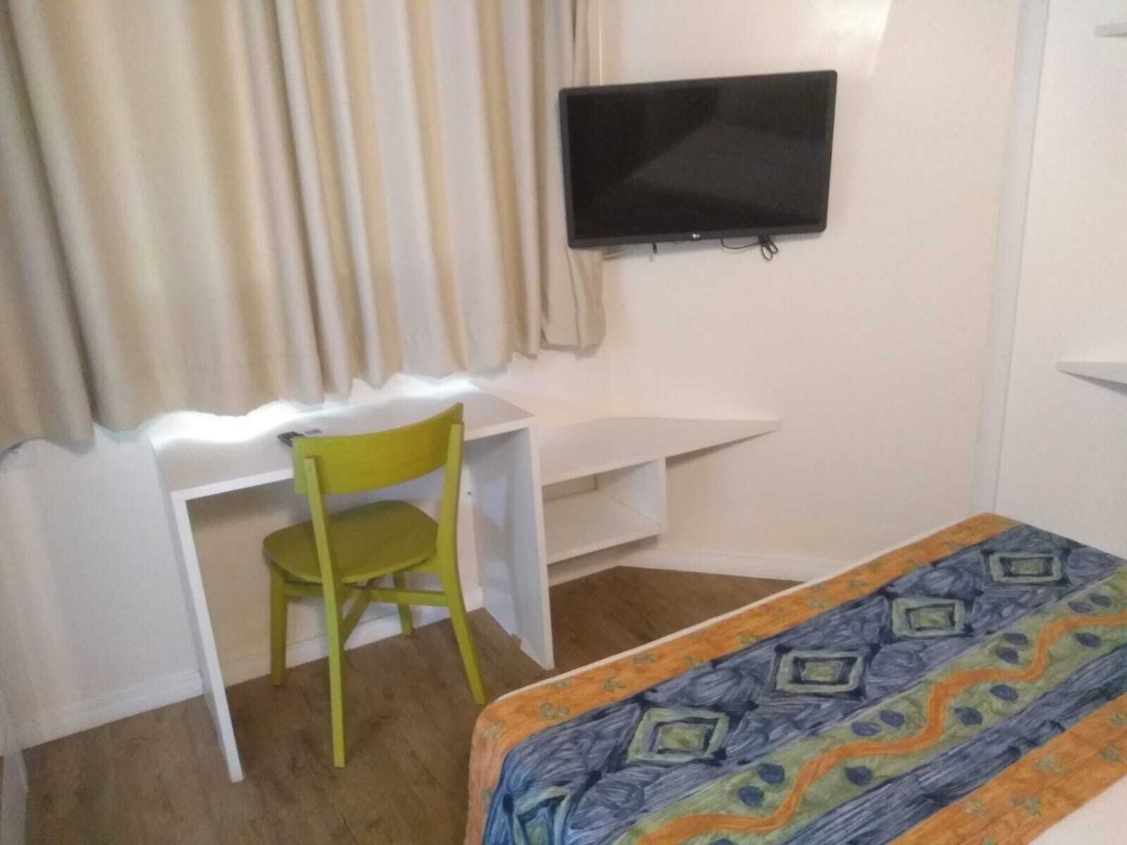 Una habitación pequeña con una cama, un escritorio, una silla y un televisor en la pared.