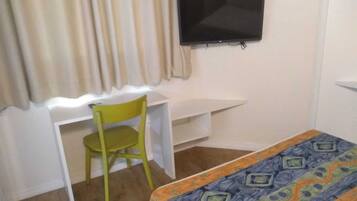 Una habitación pequeña con una cama, un escritorio, una silla y un televisor en la pared.