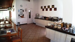 A restaurant with a dining area, a kitchen with a buffet, and a wall with fruit-themed decorations. - Hotel Pousada do Sol (Aracaju)