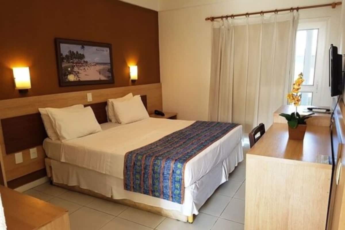 Una habitación de hotel con una cama grande, un escritorio con silla, un televisor y una ventana con cortinas.