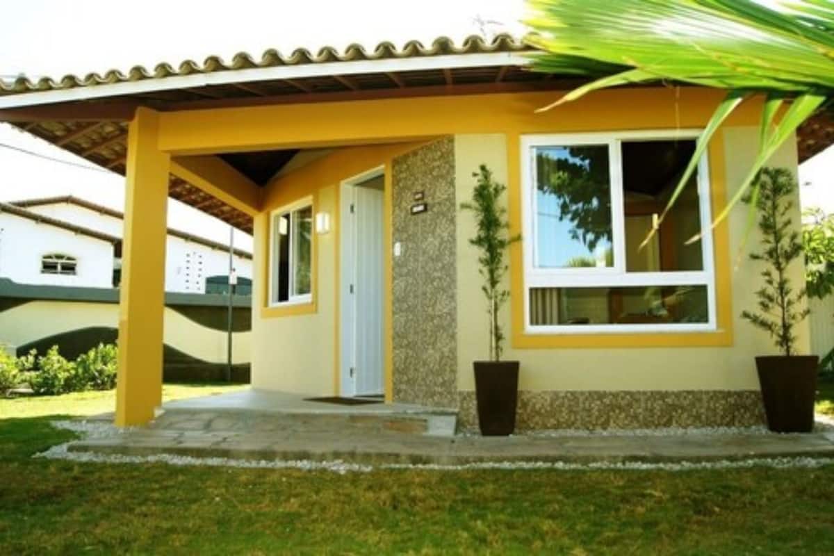 Un edificio amarillo con un porche cubierto, dos macetas y una puerta de vidrio transparente.