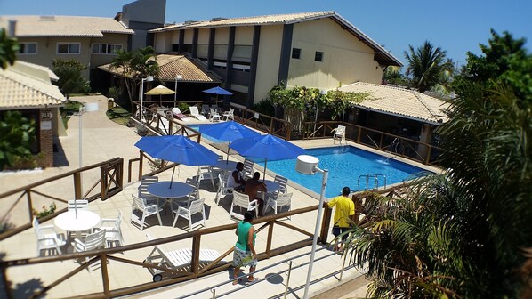 A pool area with lounge chairs and umbrellas, surrounded by buildings and greenery. - Hotel Pousada do Sol (Aracaju)