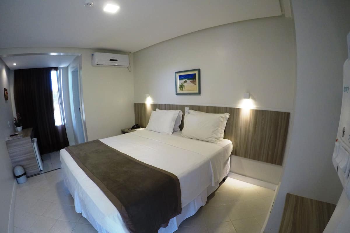 Habitación de hotel con una cama grande, una mesita de noche con lámpara, un equipo de aire acondicionado y un cuadro en la pared.