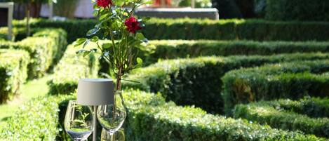 A table set outdoors with a vase of red flowers, wine glasses, and plates.