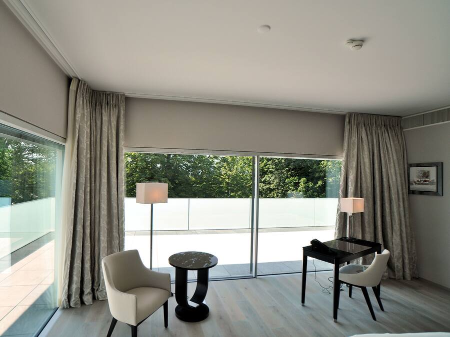 Una habitación de hotel moderna con balcón, dos sillas, una mesita y una lámpara.