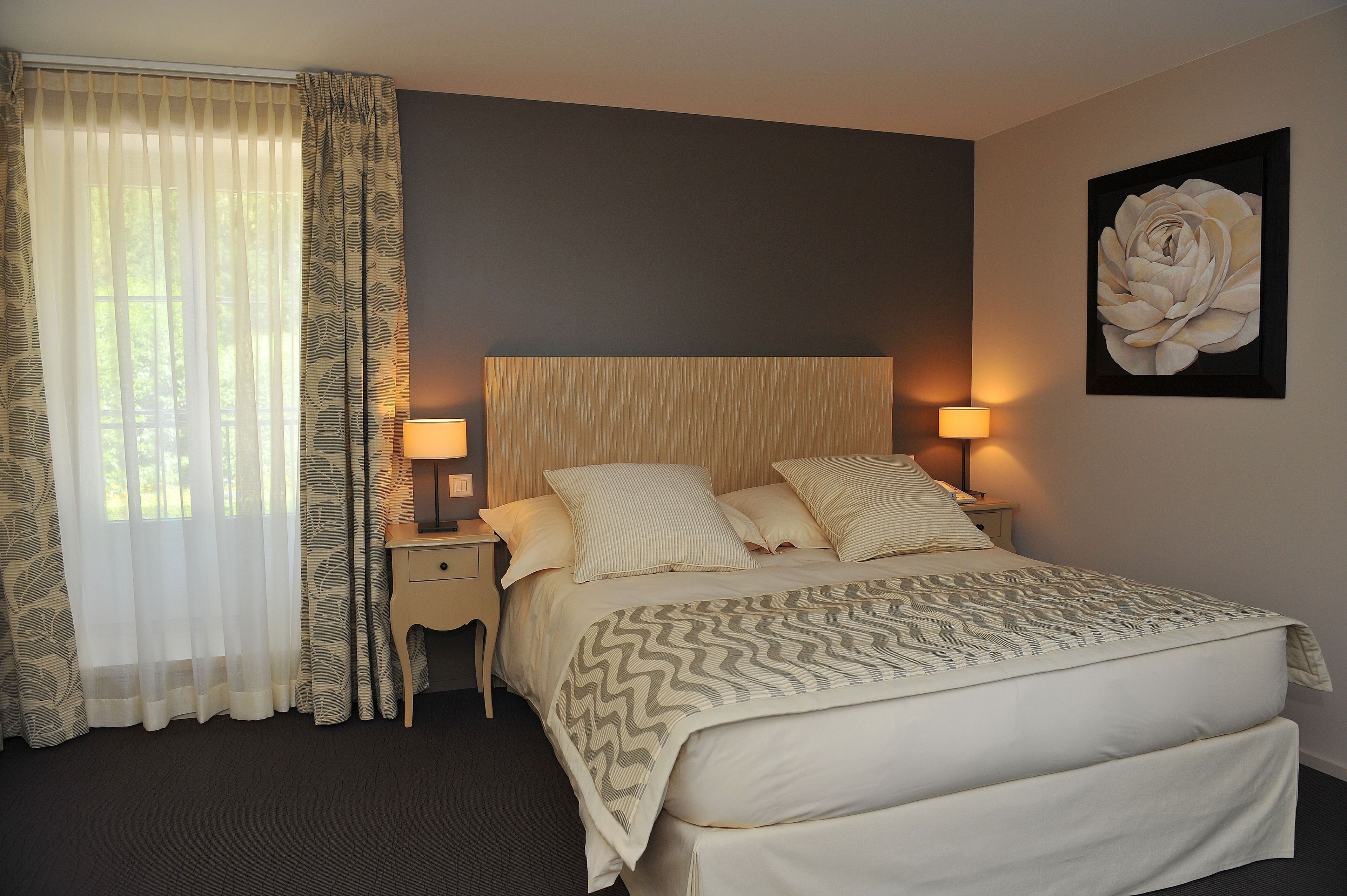 A neatly made bed with a patterned bedspread, a bedside lamp, and a large framed floral artwork on the wall.