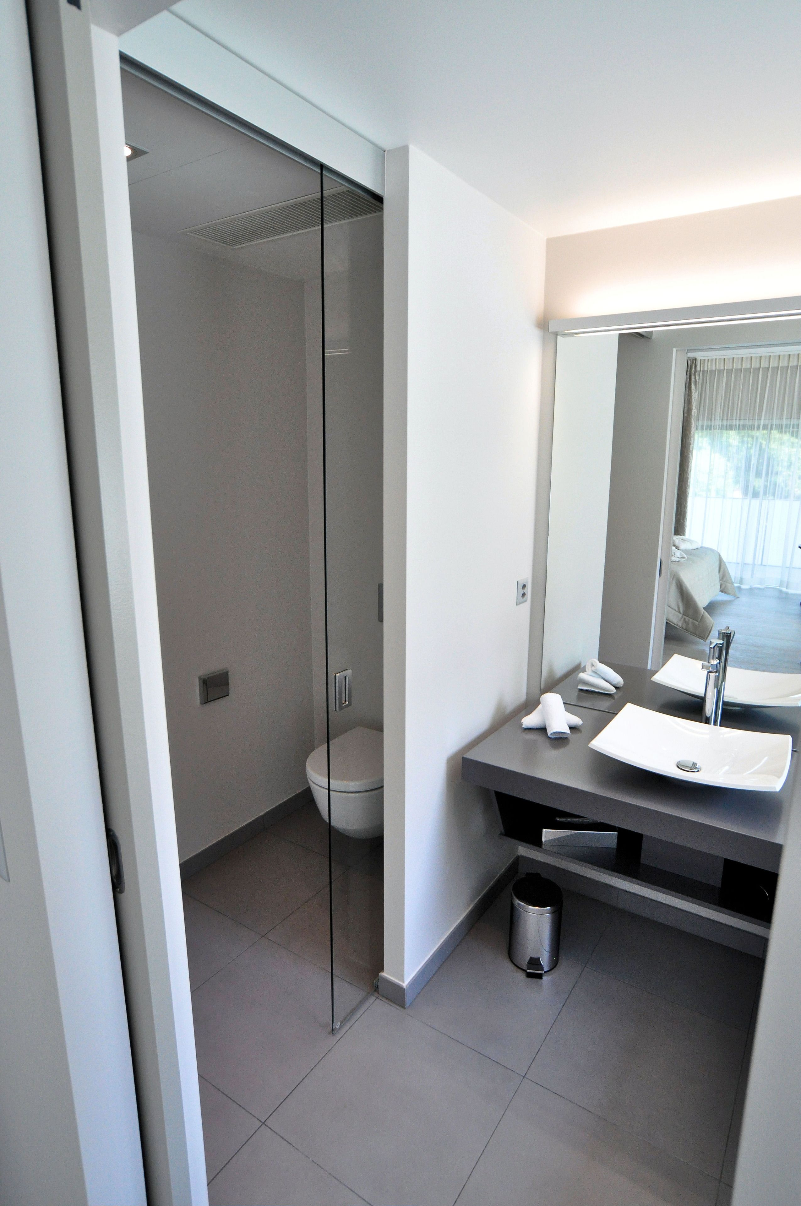 Une salle de bain moderne avec une douche à parois de verre, des toilettes blanches, un grand miroir et un lavabo avec un porte-serviette.