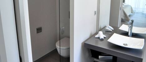 A modern bathroom with a glass shower enclosure, a white toilet, a large mirror, and a sink with a towel.