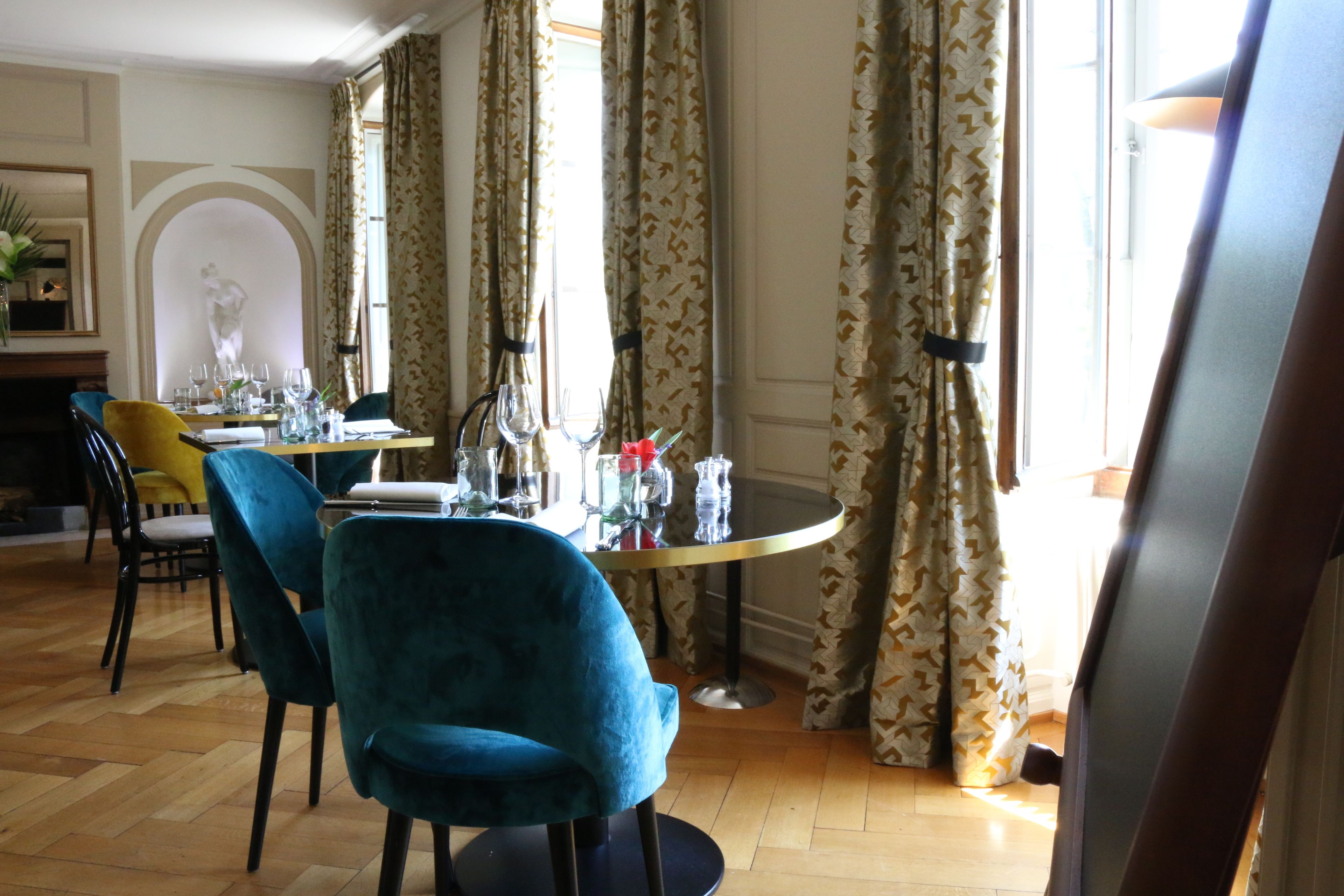 A dining area with a round table set for two, two blue chairs, and a vase with flowers.