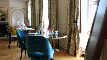 A dining area with a round table set for two, two blue chairs, and a vase with flowers.