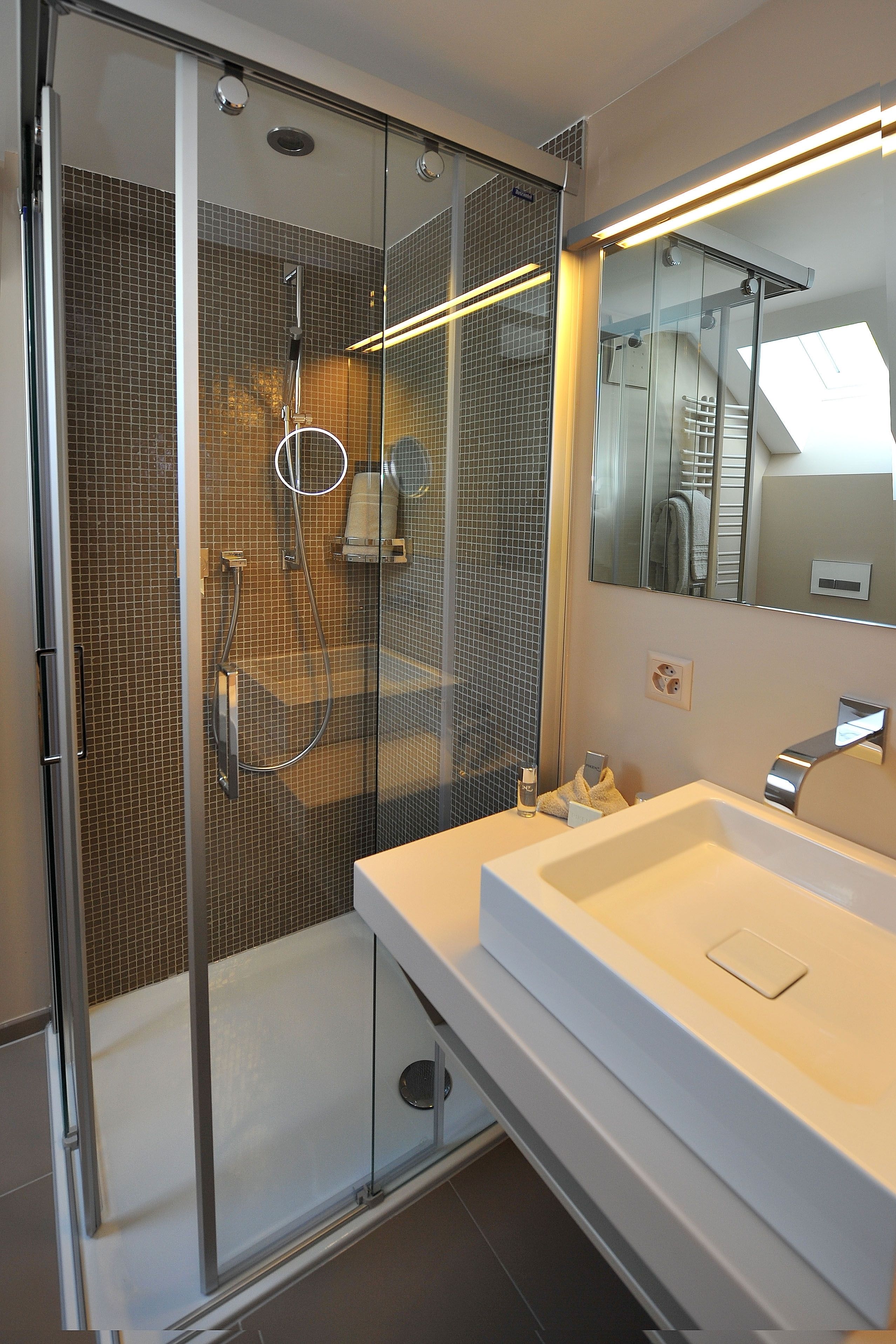 A modern bathroom with a glass-enclosed shower, a white sink, and a large mirror.