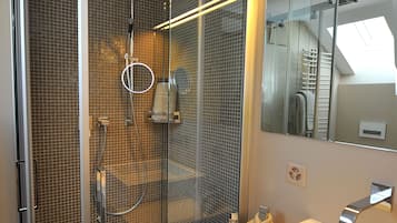 Ein modernes Badezimmer mit einer gläsernen Duschkabine, einem weißen Waschbecken und einem großen Spiegel.