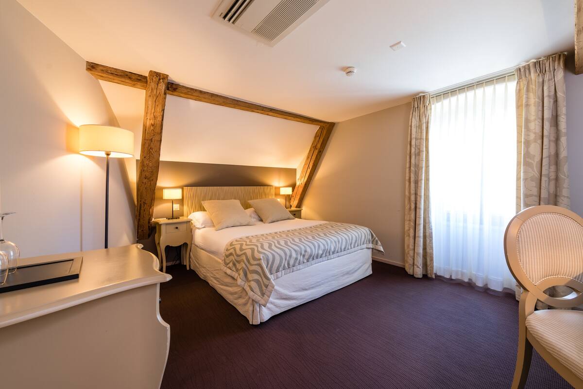 A hotel room with a bed, bedside lamps, a desk, and a chair.