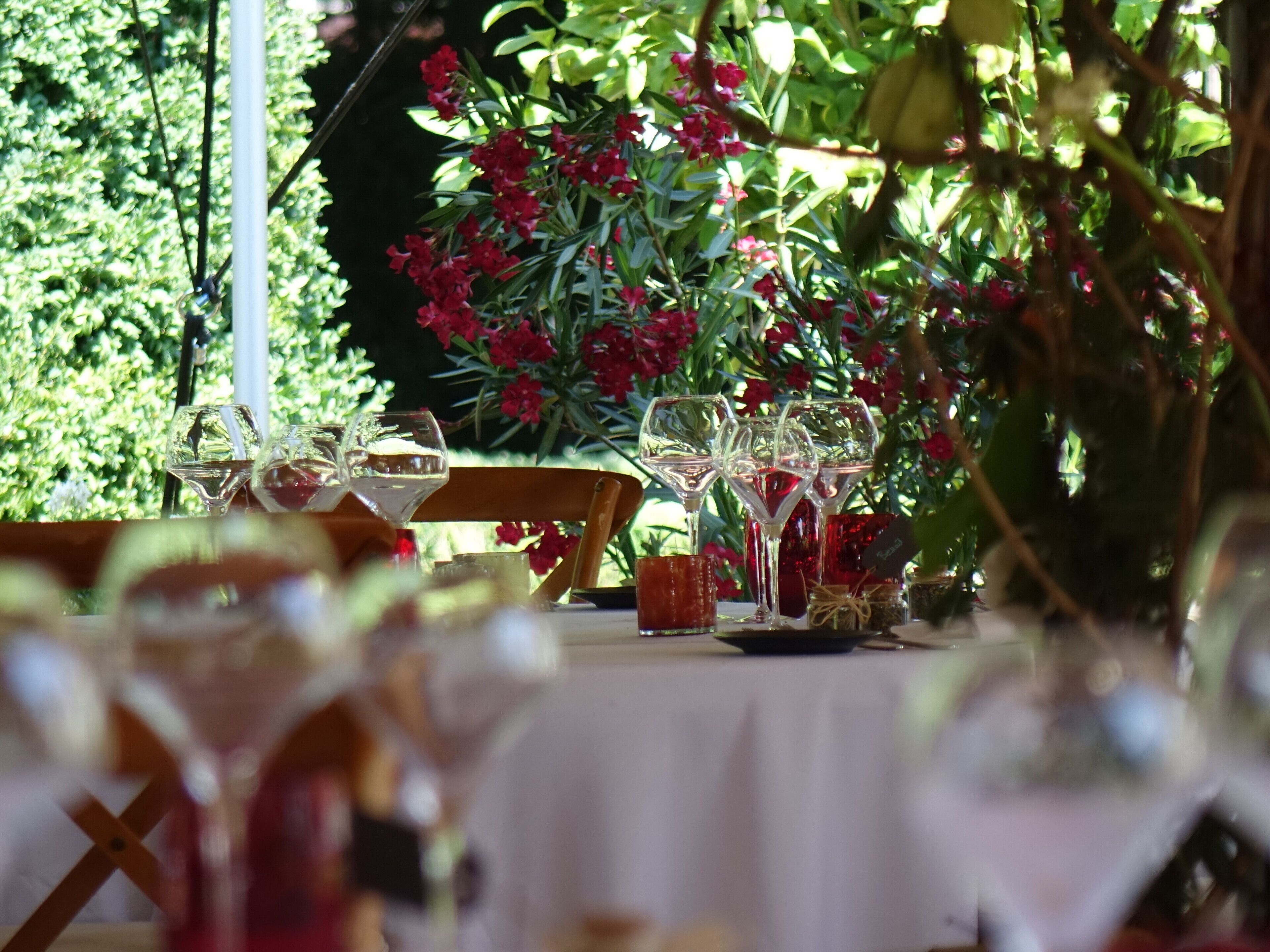 A table set for a meal with wine glasses and a red candle, surrounded by greenery and flowers.