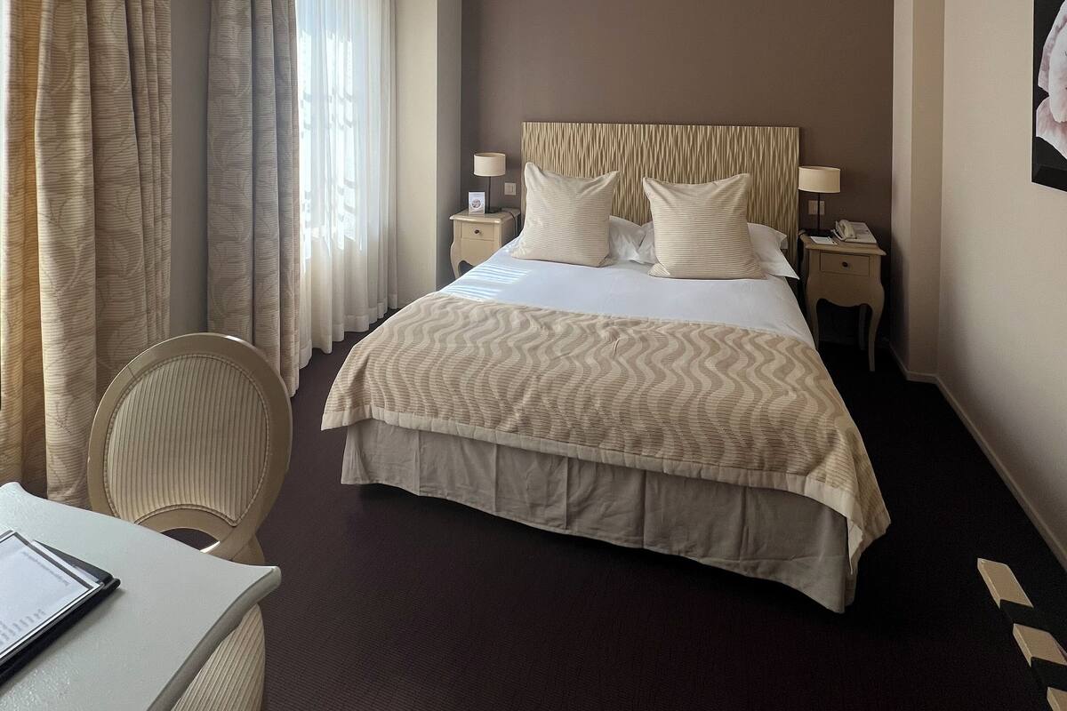 A hotel room with a large bed, two bedside tables with lamps, a chair, and a desk with a laptop.