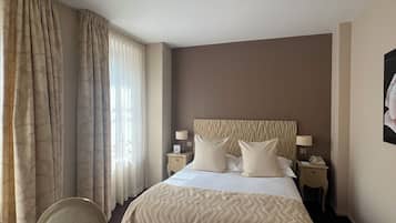 A hotel room with a large bed, two bedside tables with lamps, a chair, and a desk with a laptop.
