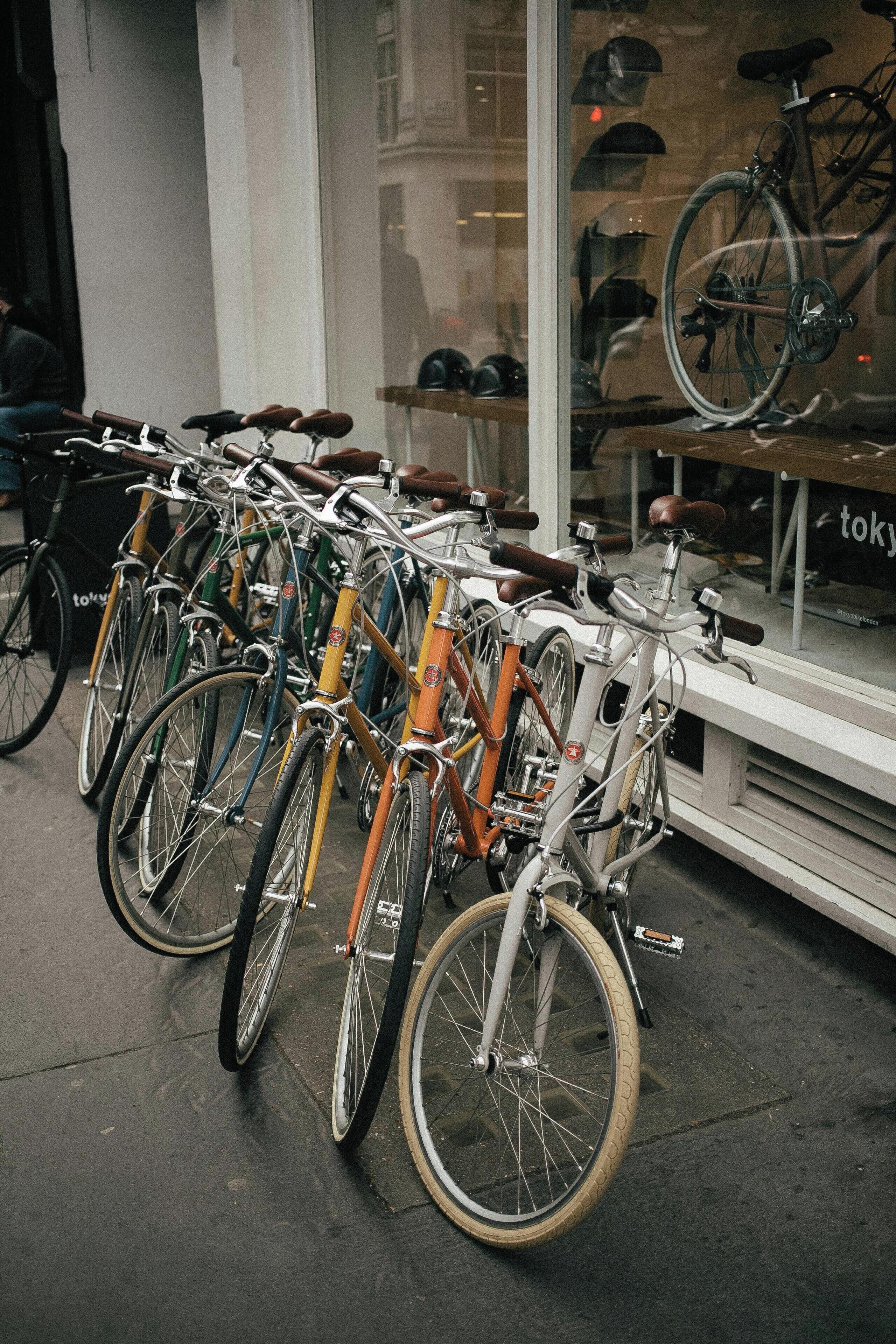 Varias bicicletas estacionadas frente a un edificio con una ventana que exhibe cascos y un letrero que dice 'tokyo'.