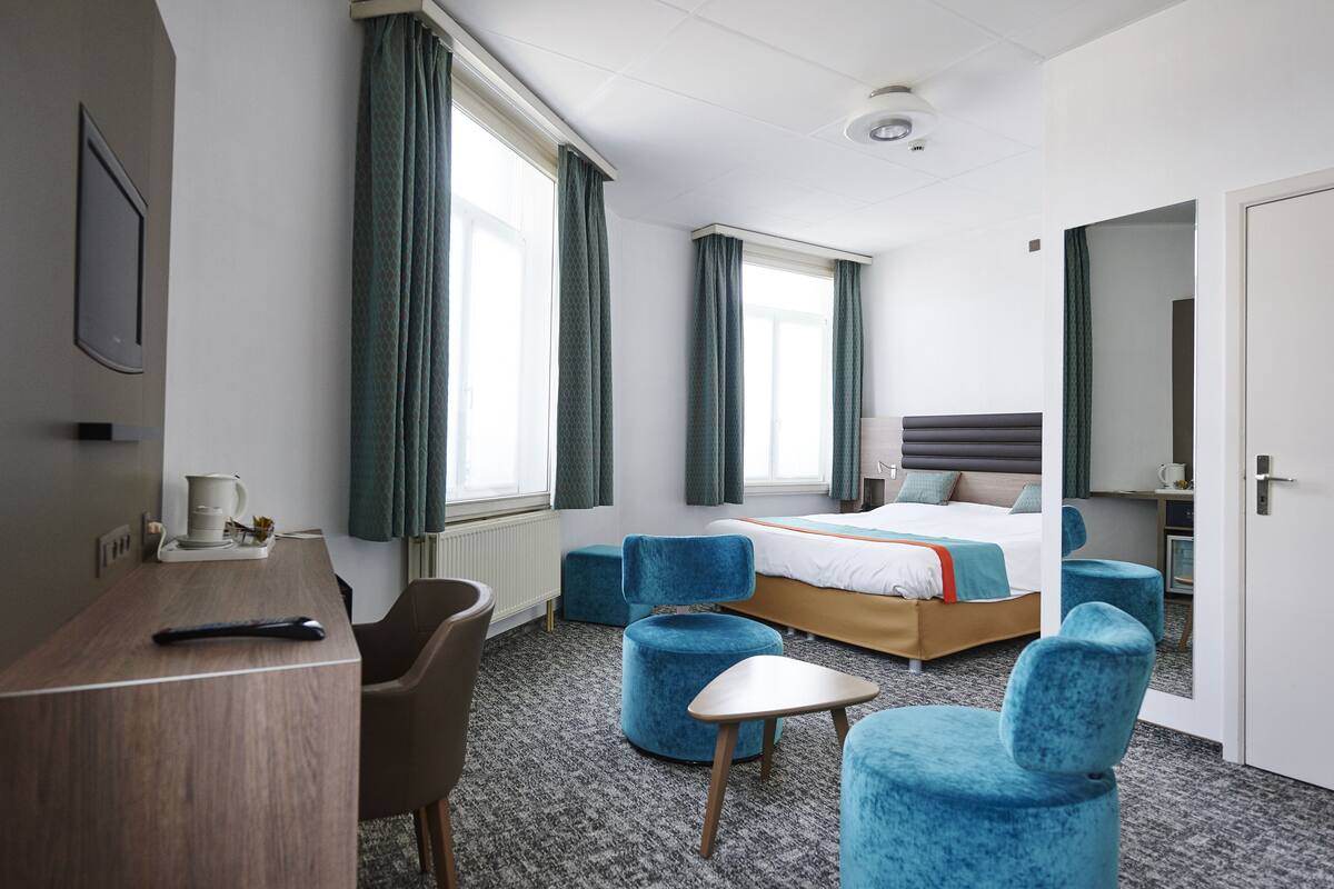 Una habitación de hotel moderna con una cama, un escritorio y dos sillones azules.