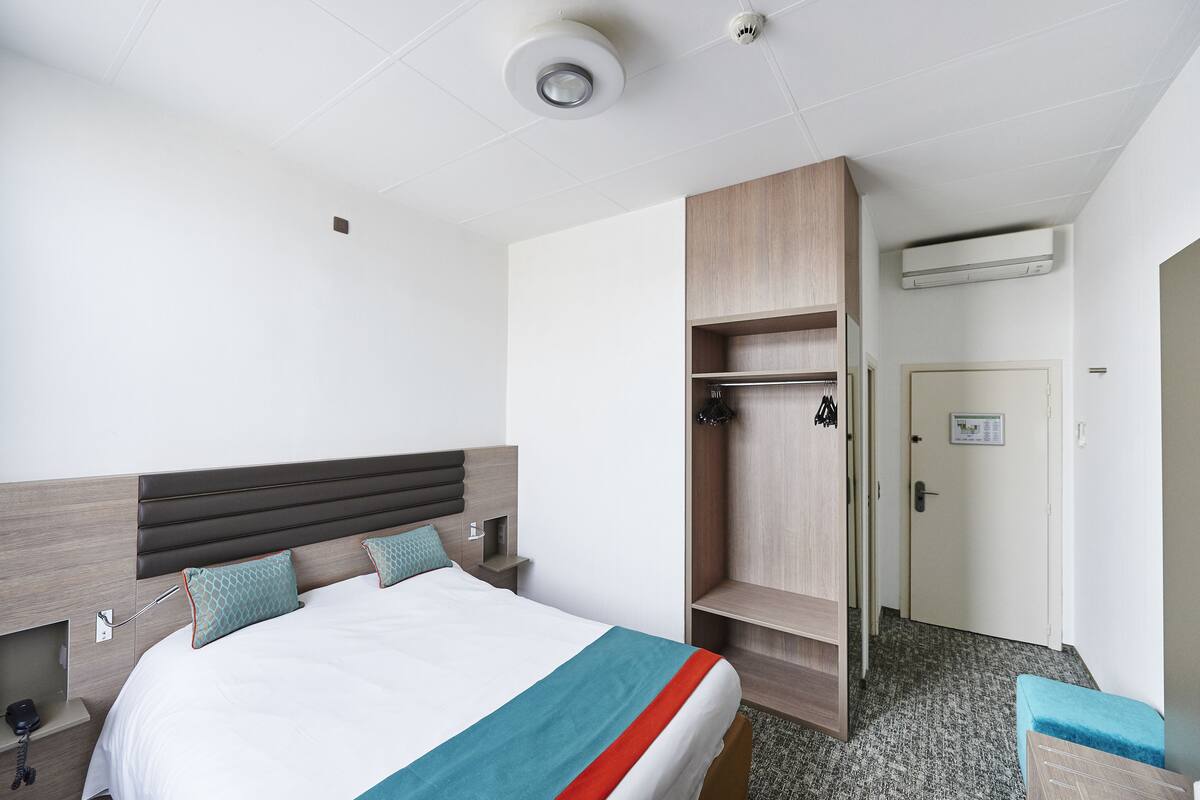 Una habitación de hotel con cama, armario, banco y una puerta con un cartel.