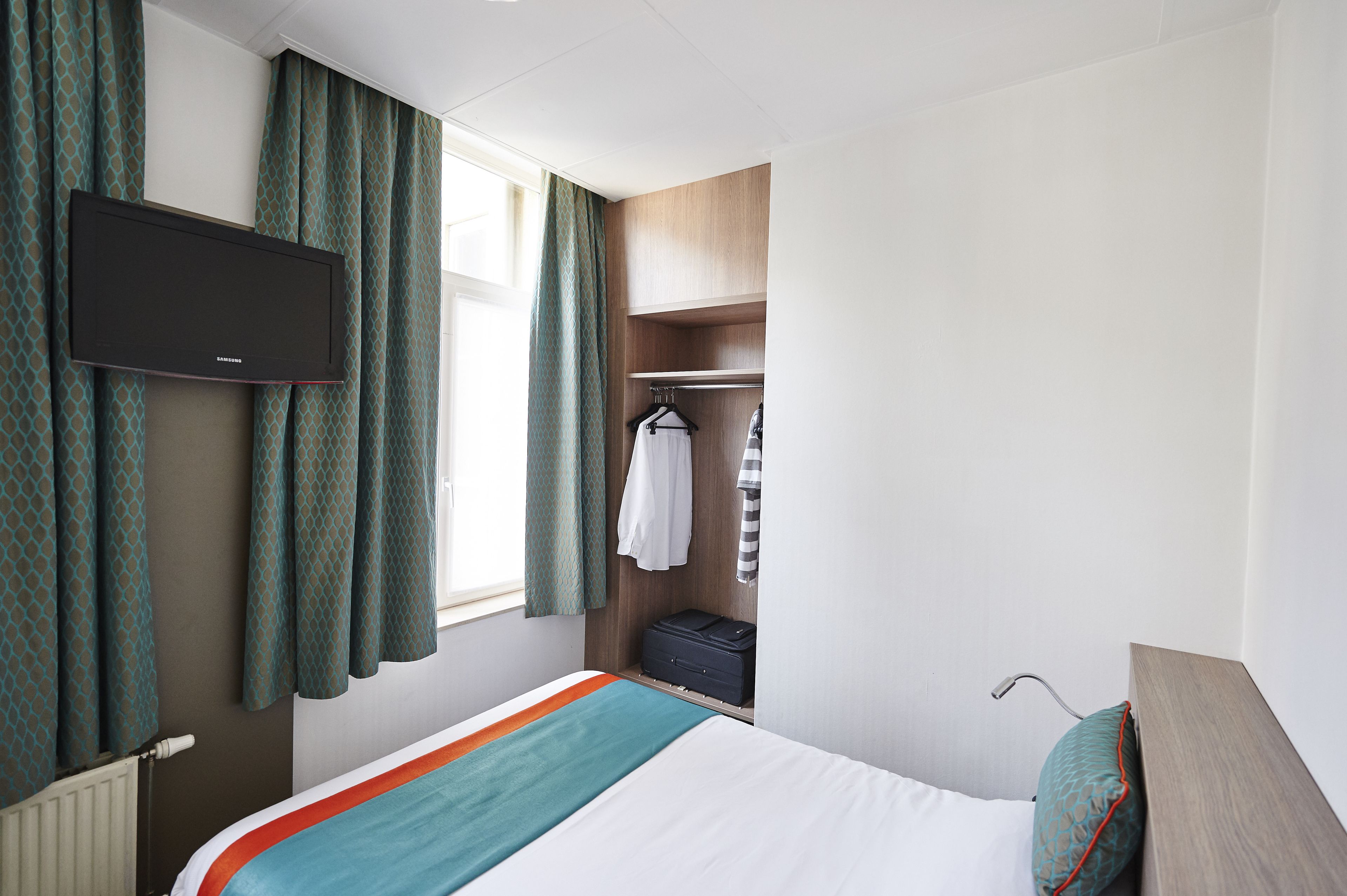 A hotel room with a bed, a wardrobe, a television, and a window with curtains.
