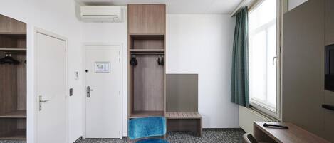 Una habitación de hotel con armario, escritorio, silla y ventana.