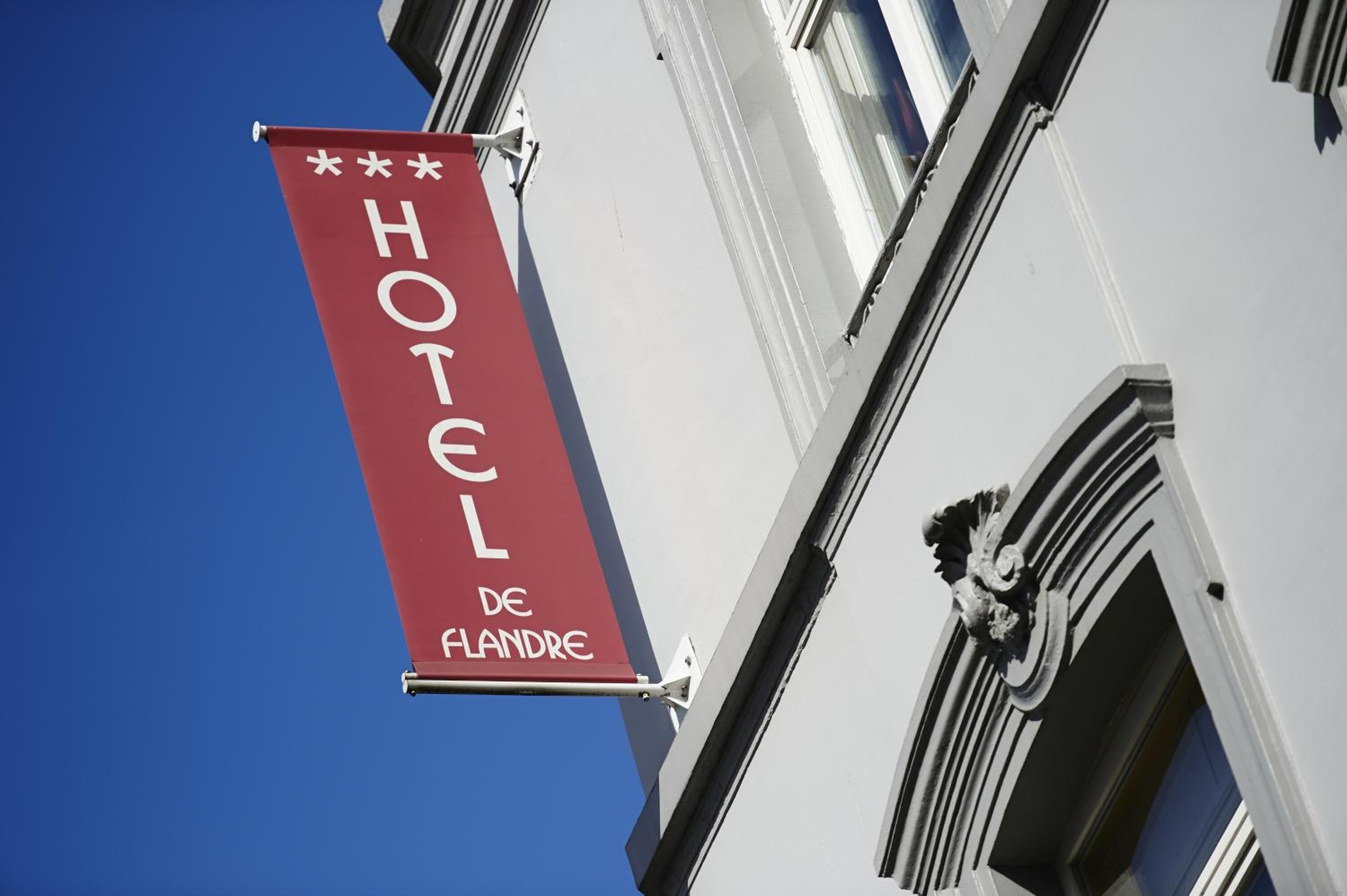 A hotel sign with the name "HOTEL DE FLANDRE" against a clear blue sky.