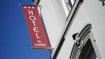 A hotel sign with the name "HOTEL DE FLANDRE" against a clear blue sky.