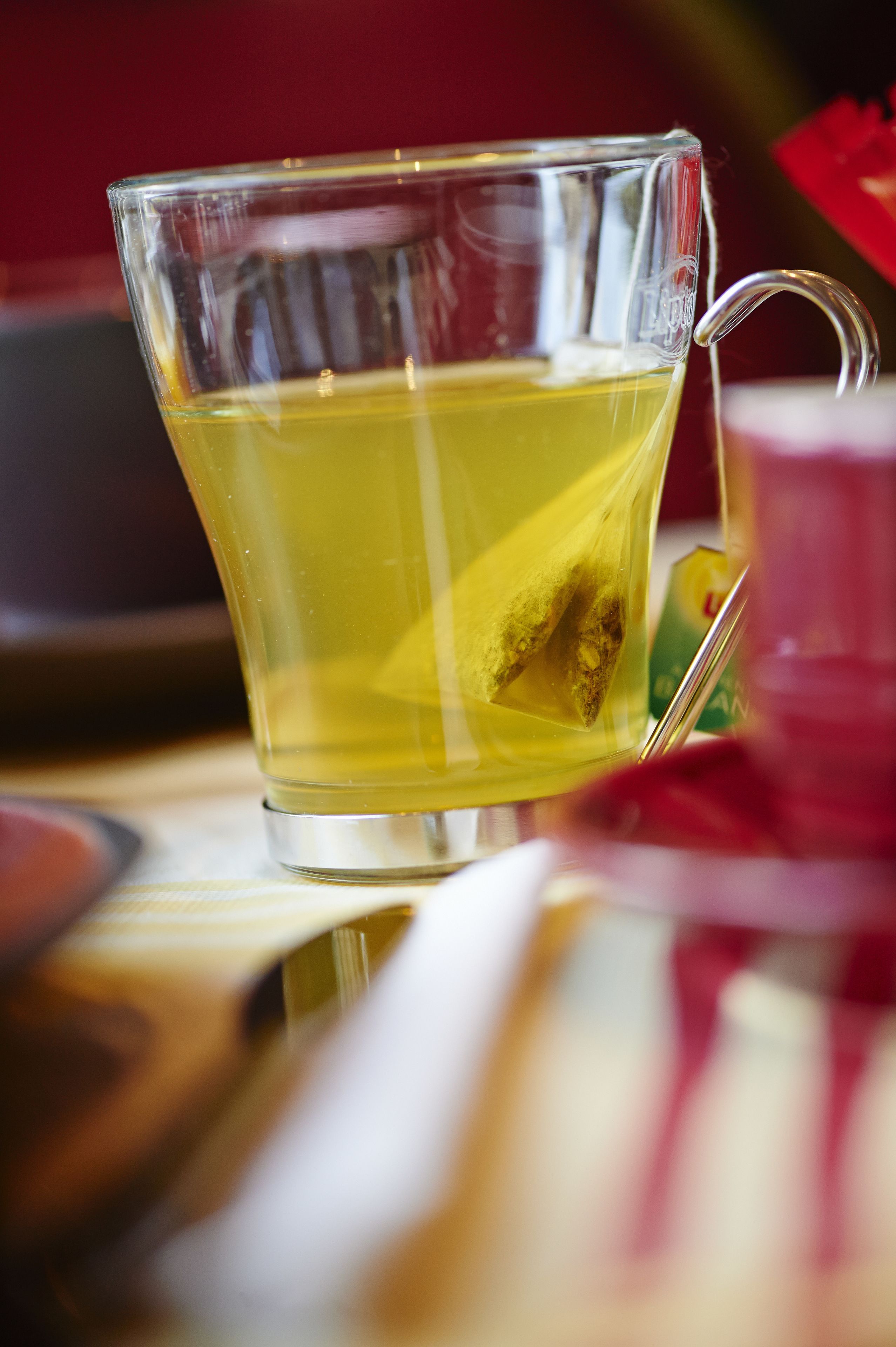 Una taza de vidrio transparente con asa, que contiene un líquido amarillo, posiblemente té, con una bolsita de té en su interior.