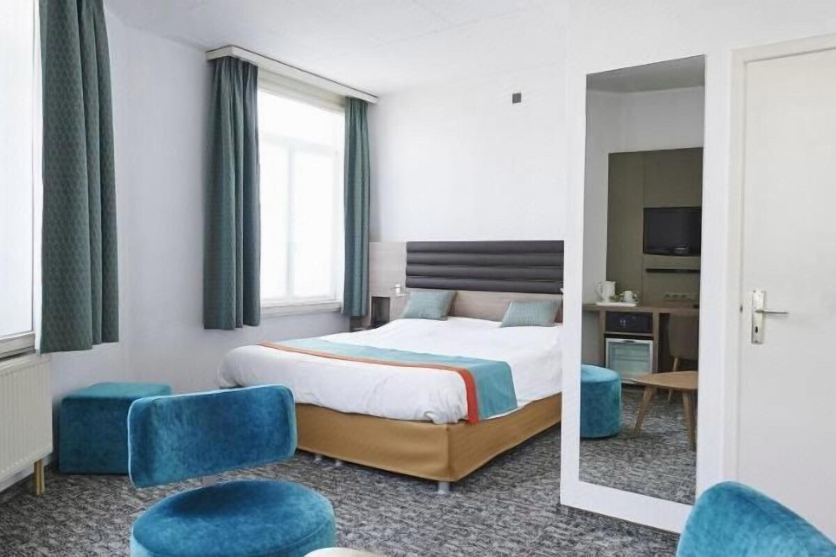 Une chambre d’hôtel avec un lit, un bureau, une chaise et un grand miroir.