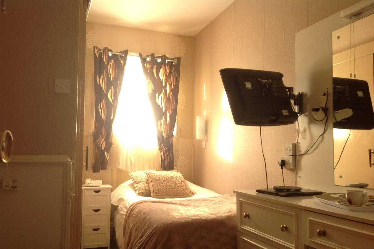 A hotel room with a bed, a bedside table, a mirror, and a window with curtains.