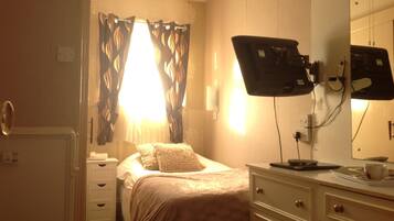 A hotel room with a bed, a bedside table, a mirror, and a window with curtains.