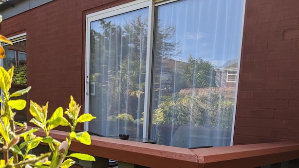 Un espace patio avec une table et des chaises, une fenêtre avec des stores et une vue sur un jardin.