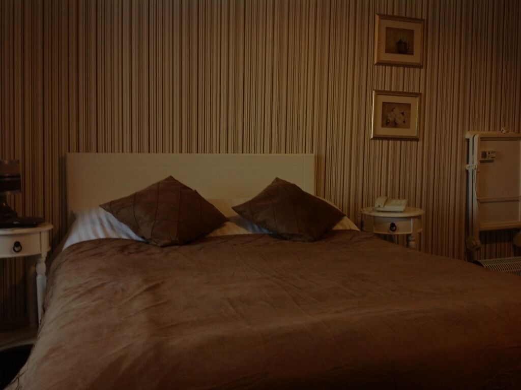 Une chambre avec un lit, deux oreillers, une table de chevet, une lampe et un mur orné de lignes verticales.