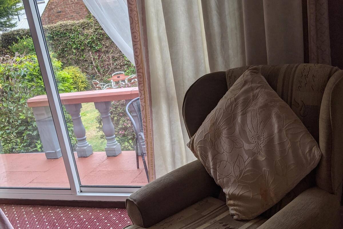 A room with a view of a garden, a sofa with a cushion, and a tray with cups and a coffee pot.
