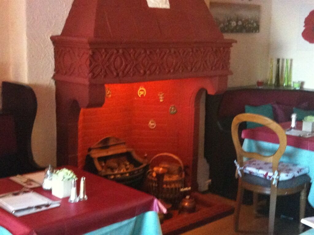 A dining area with a red fireplace, a table with a red tablecloth, and a chair with a floral cushion.